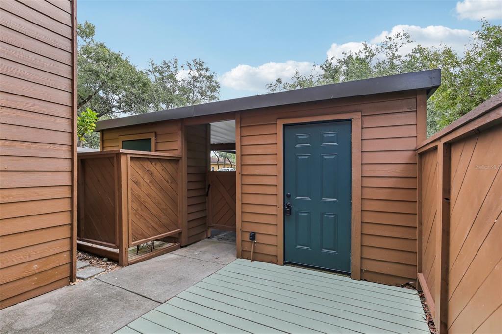 A wooden shed with a dark green door sits on a concrete patio — 2407 CYPRESS POND ROAD UNIT 2407, PALM HARBOR, FL