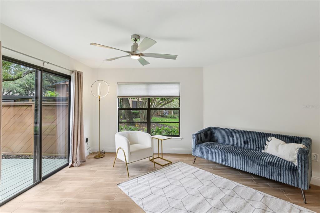 A living room features a blue velvet sofa, a white armchair, and a sliding glass door — 2407 CYPRESS POND ROAD UNIT 2407, PALM HARBOR, FL