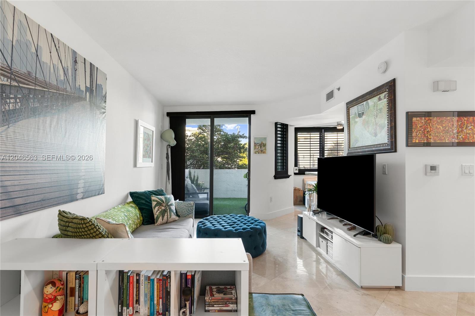 A living room features a sofa, blue ottoman, television, and a sliding door to a balcony — 110 Washington Ave # 2309, Miami Beach FL 33139, MIAMI BEACH, FL