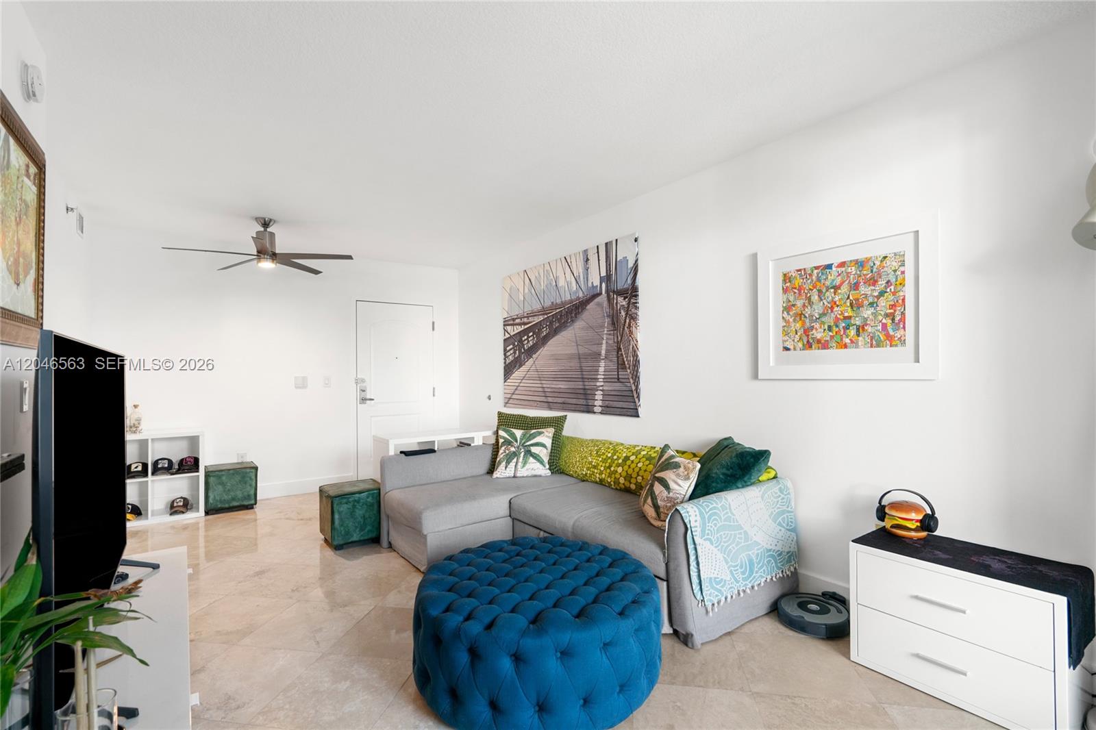 A living room features a gray sectional sofa, a large blue tufted ottoman, and tile flooring — 110 Washington Ave # 2309, Miami Beach FL 33139, MIAMI BEACH, FL