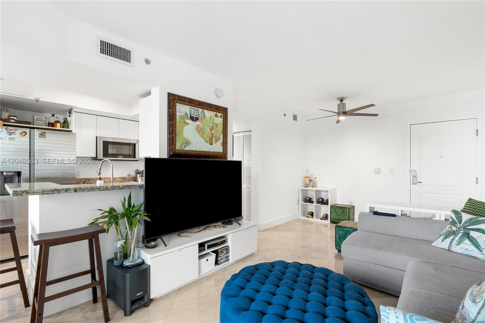 A living room features a large television, a blue tufted ottoman, and an open kitchen — 110 Washington Ave # 2309, Miami Beach FL 33139, MIAMI BEACH, FL