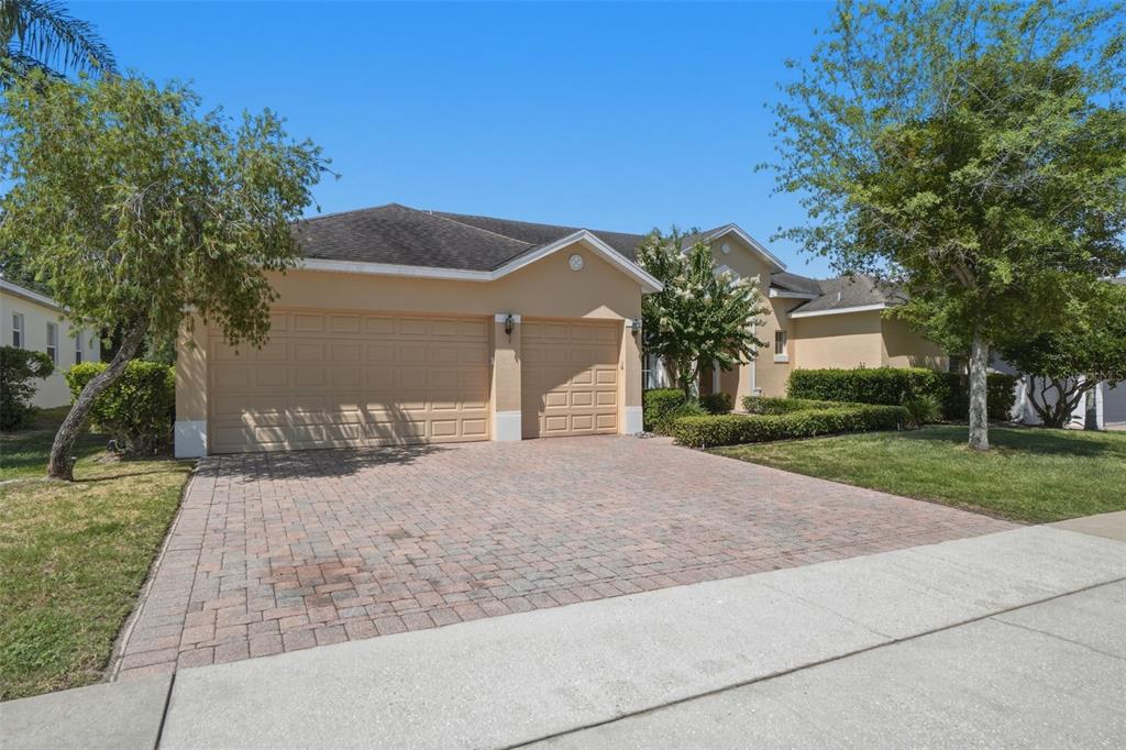 A tan single-story house features a three-car garage and a paved driveway — 2330 PESARO CIRCLE, OCOEE, FL