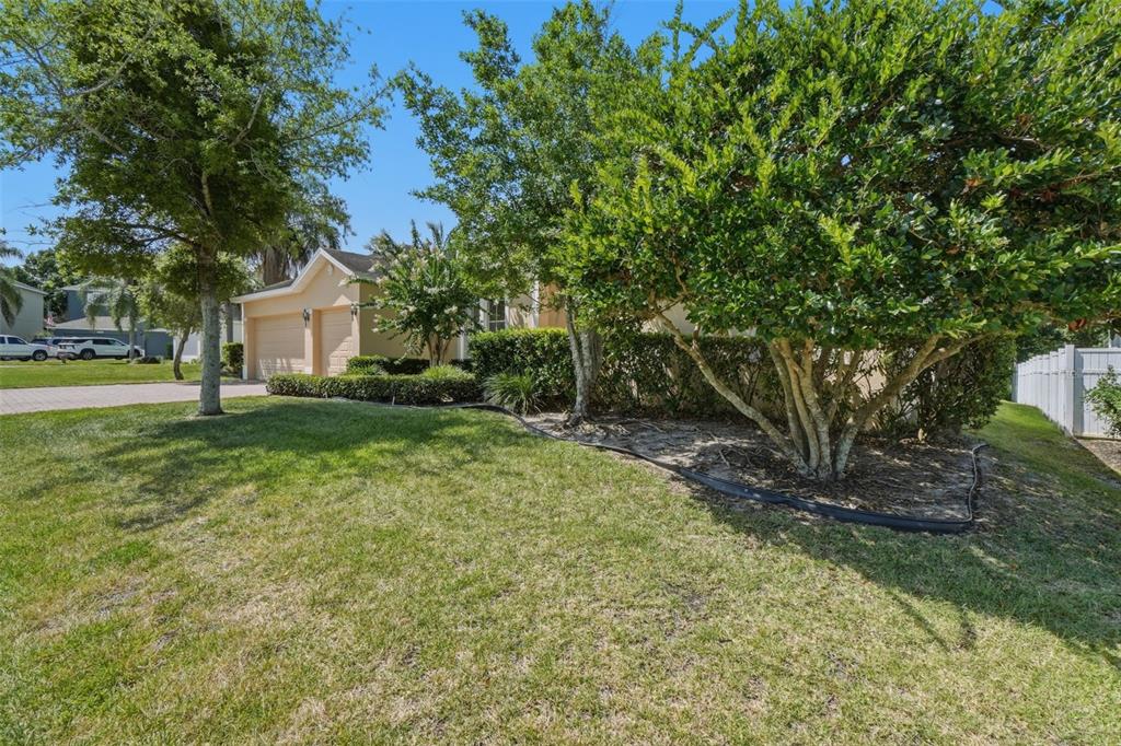 A tan house with a two-car garage is partially obscured by trees and landscaping — 2330 PESARO CIRCLE, OCOEE, FL