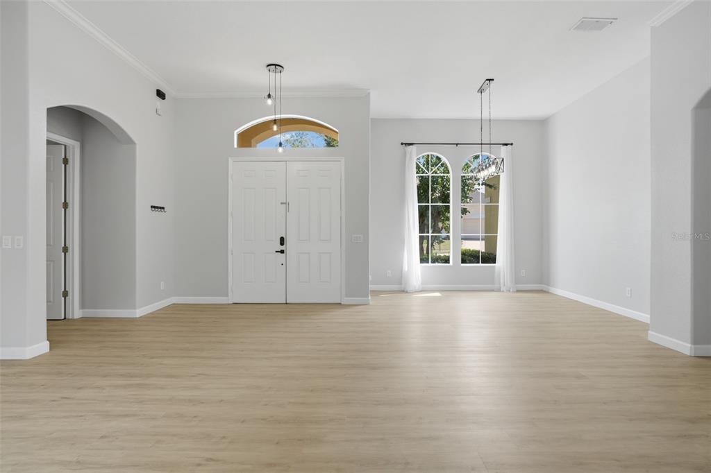 An empty room with light wood-look flooring, white walls, a double front door, and arched windows — 2330 PESARO CIRCLE, OCOEE, FL
