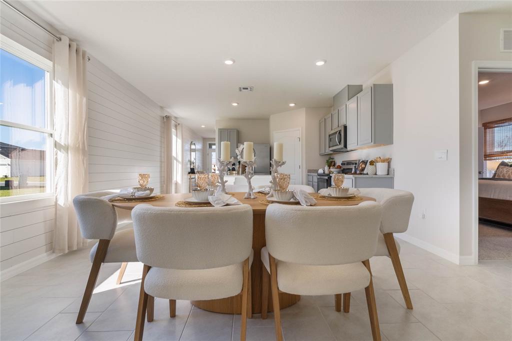 A dining area with a round wooden table and white chairs sits before a kitchen — 3034 VICEROY COURT, POINCIANA, FL