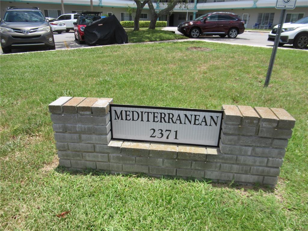 A brick sign displaying the name Mediterranean and the number 2371 sits on a lawn — 2371 ISRAELI DRIVE UNIT 67, CLEARWATER, FL