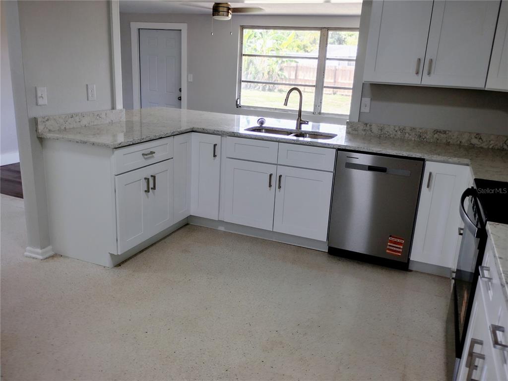 A kitchen features white cabinets, granite countertops, and stainless steel appliances over a concrete floor — 5004 22ND AVENUE W, BRADENTON, FL