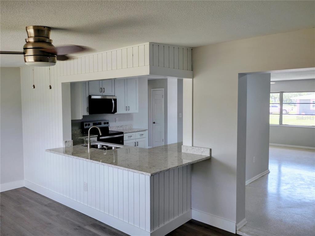 A kitchen with a breakfast bar, white cabinetry, and light countertops opens to a living area — 5004 22ND AVENUE W, BRADENTON, FL