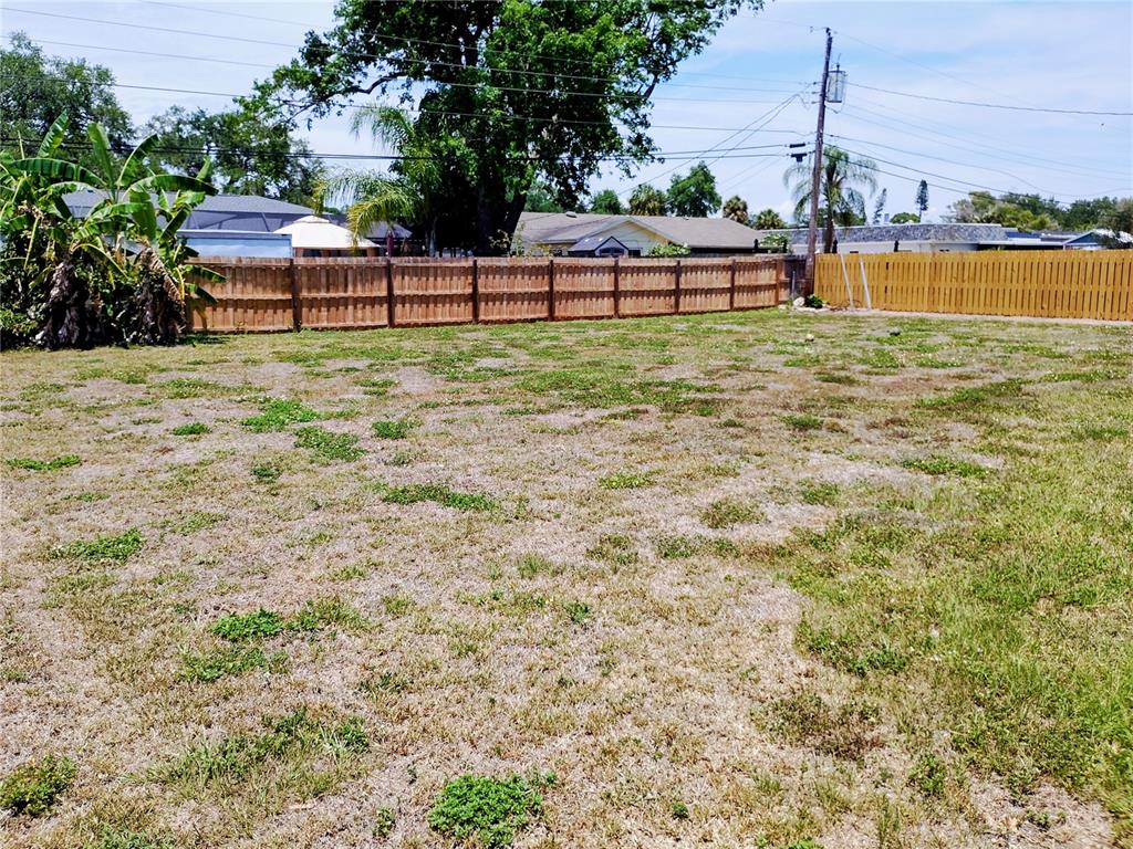 A large, flat, grassy backyard features a wooden privacy fence and several mature trees — 5004 22ND AVENUE W, BRADENTON, FL