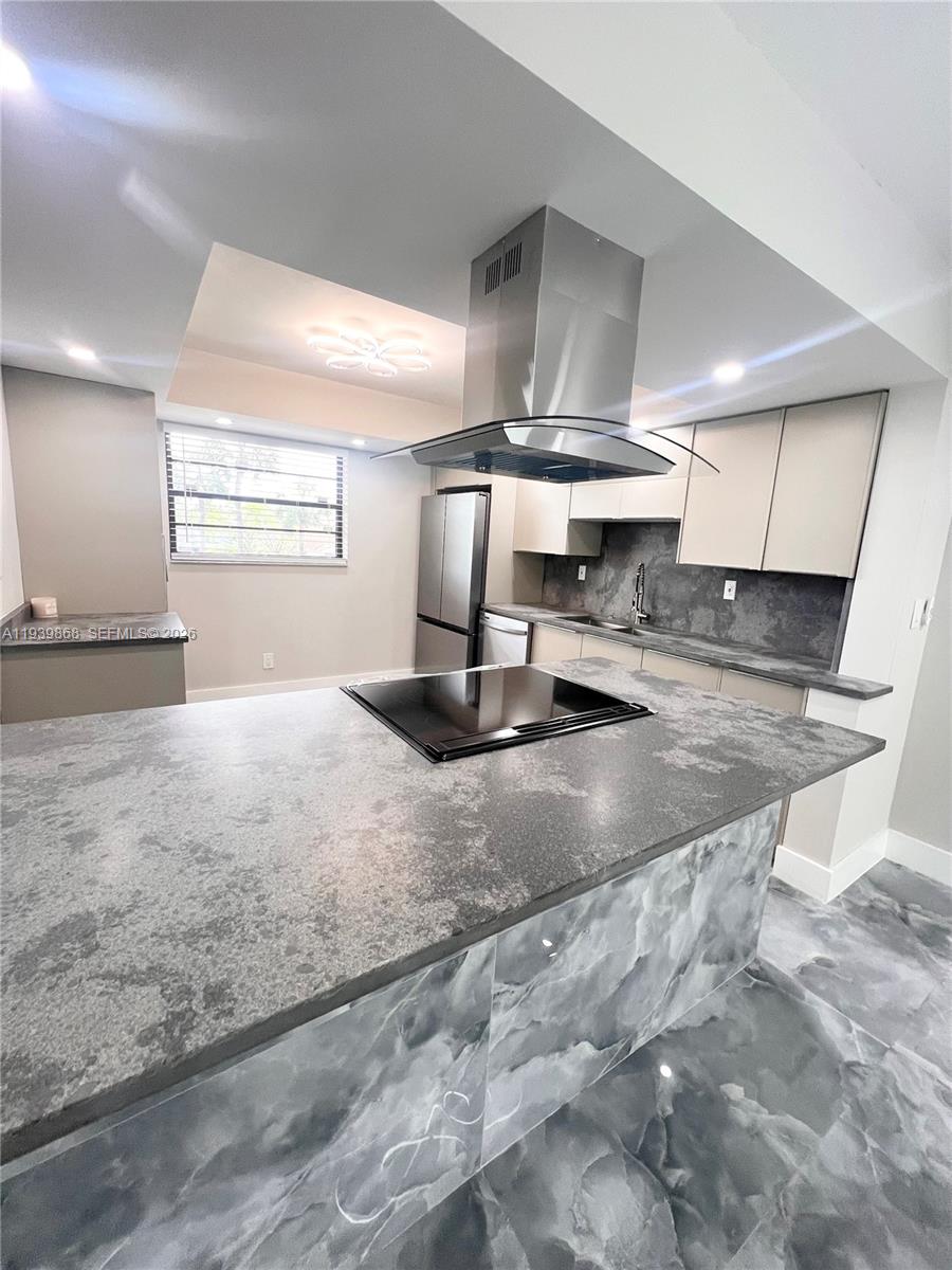 A modern kitchen features a central island with a cooktop, stainless steel hood, and marble-patterned flooring — 4930 E Sabal Palm Blvd # 206, Tamarac FL 33319, TAMARAC, FL