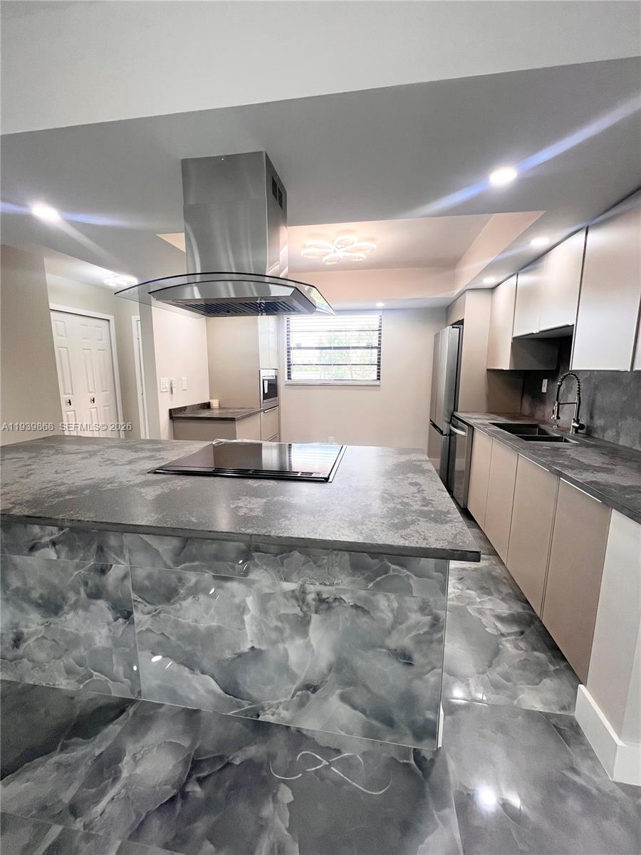 A modern kitchen features a marble-patterned island, stainless steel appliances, and sleek cabinetry — 4930 E Sabal Palm Blvd # 206, Tamarac FL 33319, TAMARAC, FL