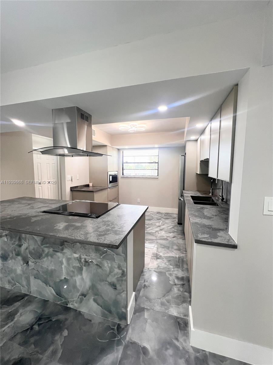 A modern kitchen features a marble-patterned island, stainless steel range hood, and gray cabinetry — 4930 E Sabal Palm Blvd # 206, Tamarac FL 33319, TAMARAC, FL