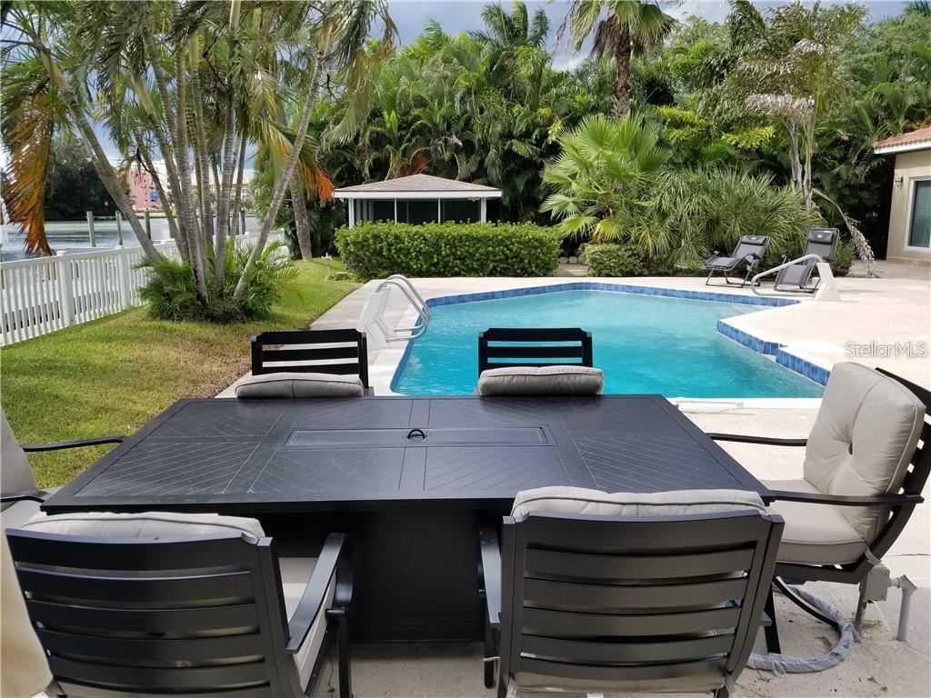A patio with a dining table and chairs overlooks a swimming pool and tropical landscaping — 4000 BELLE VISTA DRIVE, ST PETERSBURG, FL