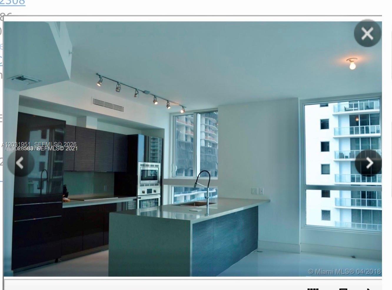 A modern kitchen features dark cabinetry, a central island with a sink, and floor-to-ceiling windows — MIAMI, FL