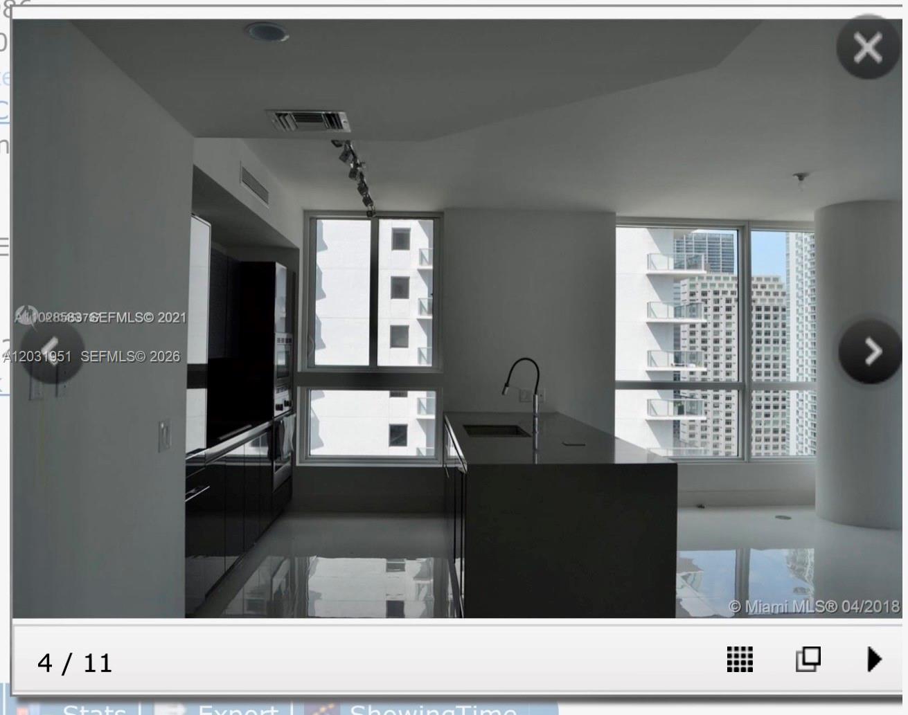 A modern kitchen features dark cabinetry, a central island with a sink, and floor-to-ceiling windows — MIAMI, FL