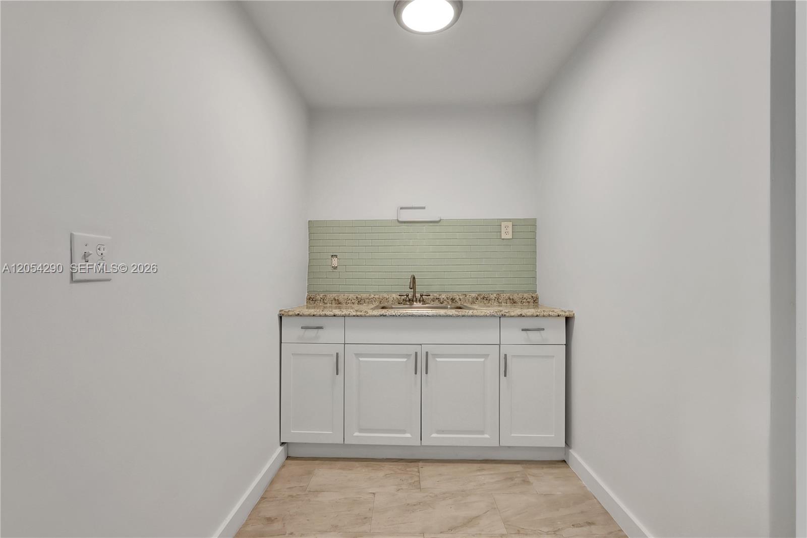 A small laundry room features white cabinets, a granite countertop, and a green tiled backsplash — 7000 NW 2 Ave # 7010, Miami FL 33150, MIAMI, FL