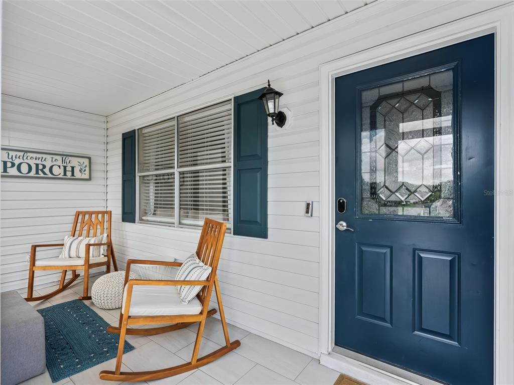 A covered front porch features white siding, a blue door, and two wooden rocking chairs — 321 SAN MARINO DRIVE, THE VILLAGES, FL
