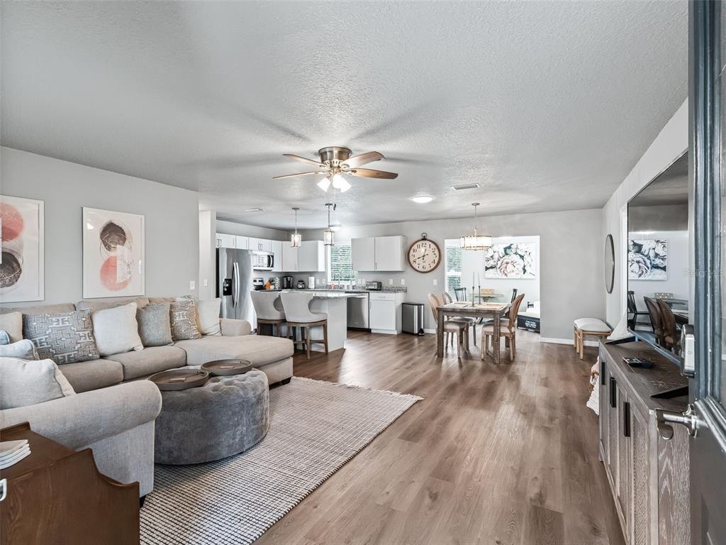 An open-concept living room and kitchen feature light gray walls and wood-look flooring — 321 SAN MARINO DRIVE, THE VILLAGES, FL