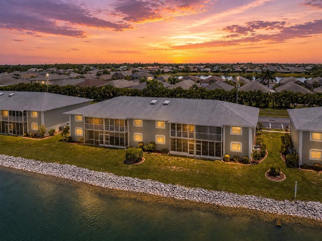 An aerial view shows multi-story apartment buildings situated along a lake at sunset — 3310 LOVELAND BOULEVARD UNIT 506, PUNTA GORDA, FL