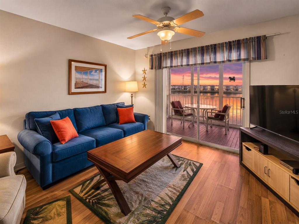A living room with a blue sofa, wooden coffee table, and a balcony overlooking water — 3310 LOVELAND BOULEVARD UNIT 506, PUNTA GORDA, FL