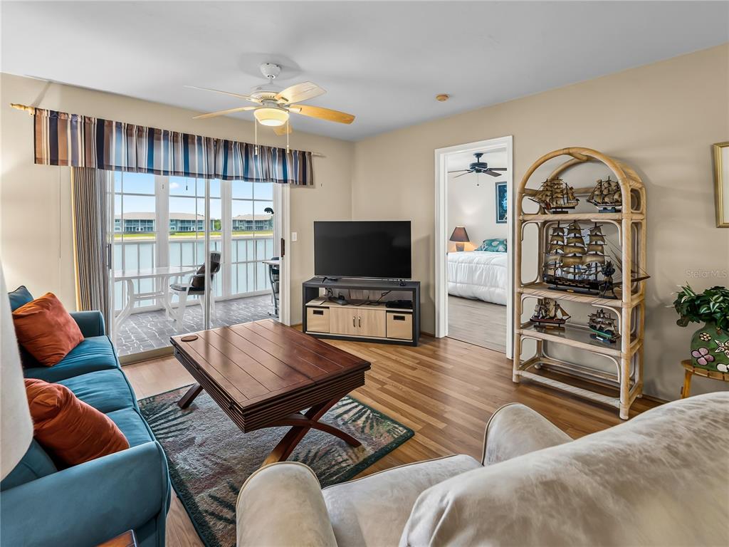 A living room features a blue sofa, wood coffee table, television, and a rattan shelf — 3310 LOVELAND BOULEVARD UNIT 506, PUNTA GORDA, FL