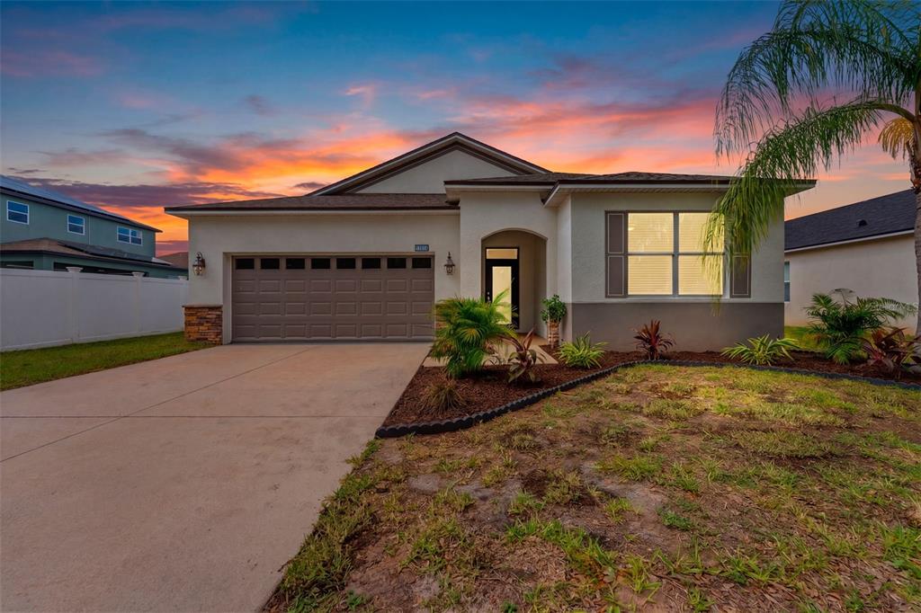 A single-story house with a two-car garage and a landscaped front yard at sunset — 11514 ASHTON FIELD AVENUE, RIVERVIEW, FL