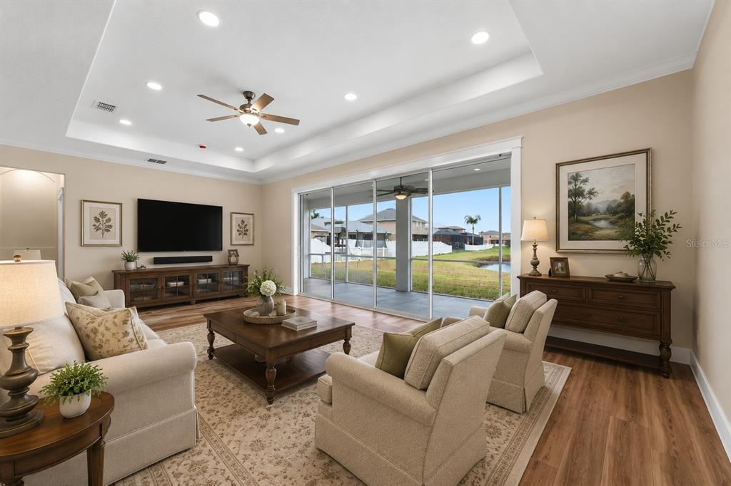 A living room with a tray ceiling, sliding glass doors, and views of a pond — 11514 ASHTON FIELD AVENUE, RIVERVIEW, FL