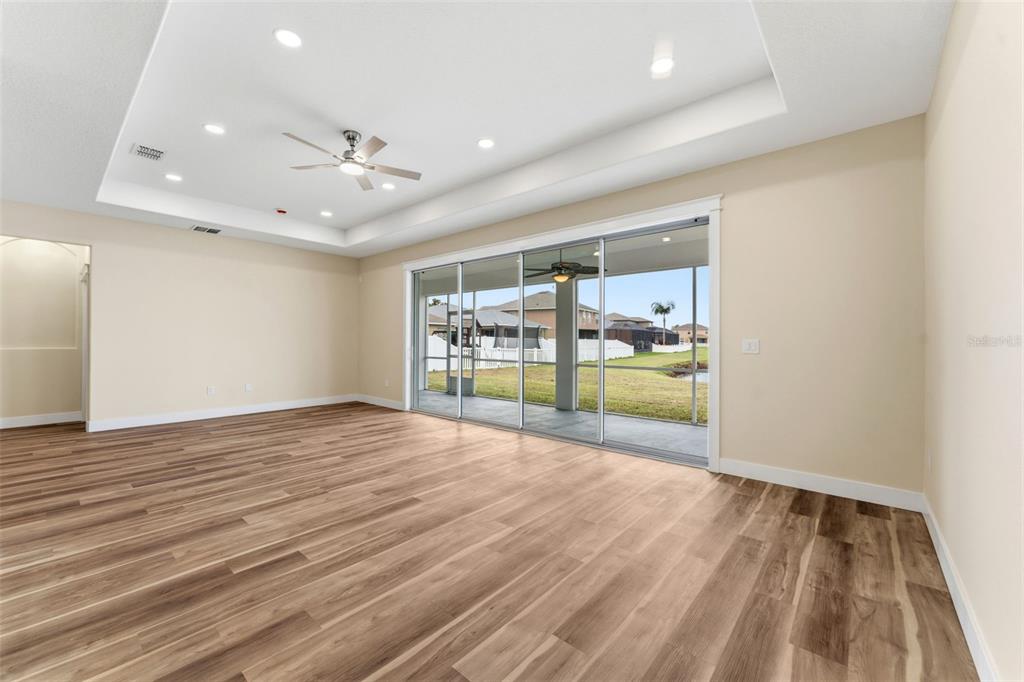 A spacious living room features a tray ceiling, wood-look flooring, and large sliding glass doors — 11514 ASHTON FIELD AVENUE, RIVERVIEW, FL