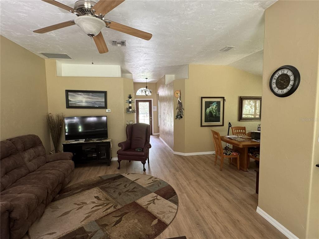 A living room with a brown sofa, television, armchair, and dining area with wood flooring — 13350 SW 61ST PLACE ROAD, OCALA, FL