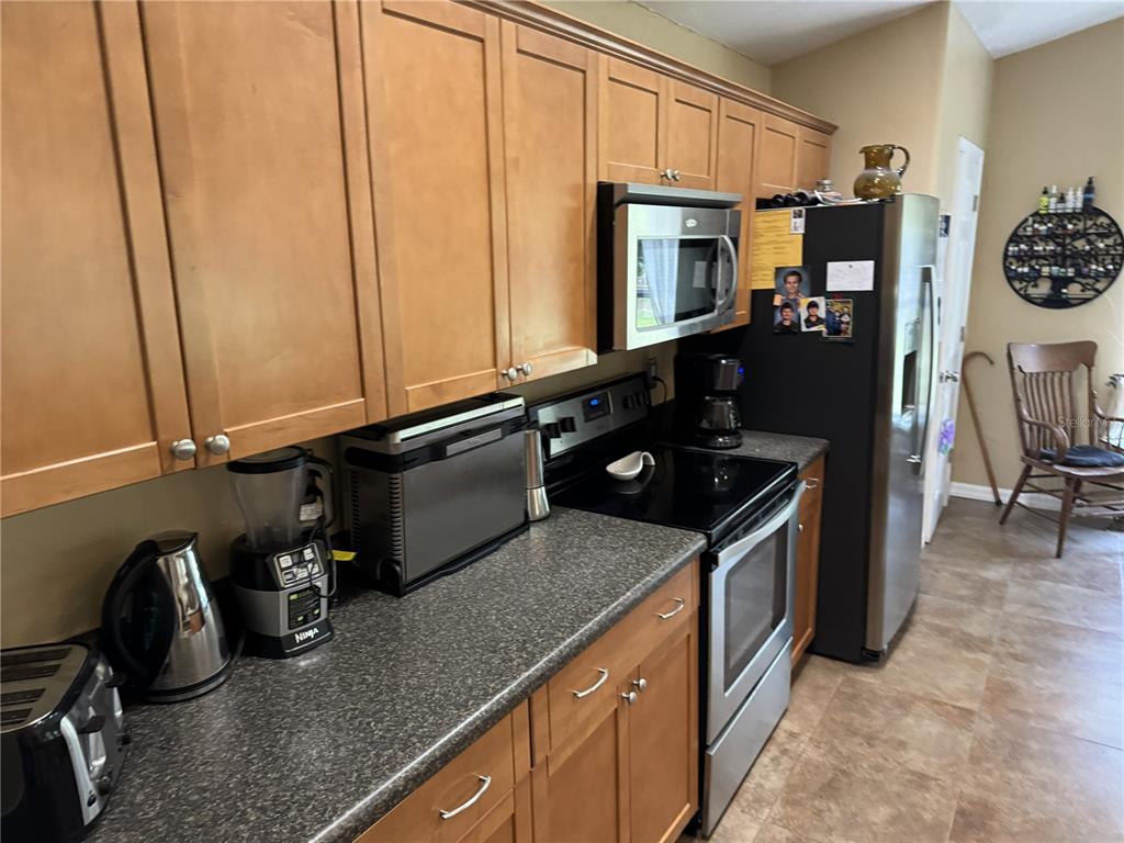 A kitchen features wooden cabinets, dark countertops, stainless steel appliances, and a black refrigerator — 13350 SW 61ST PLACE ROAD, OCALA, FL