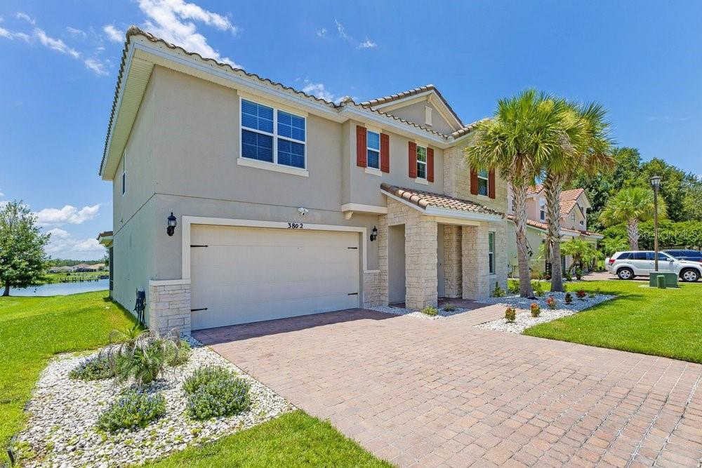 A two-story suburban house with a beige stucco exterior, stone accents, and a paved driveway — 3802 CARRICK BEND DRIVE, KISSIMMEE, FL