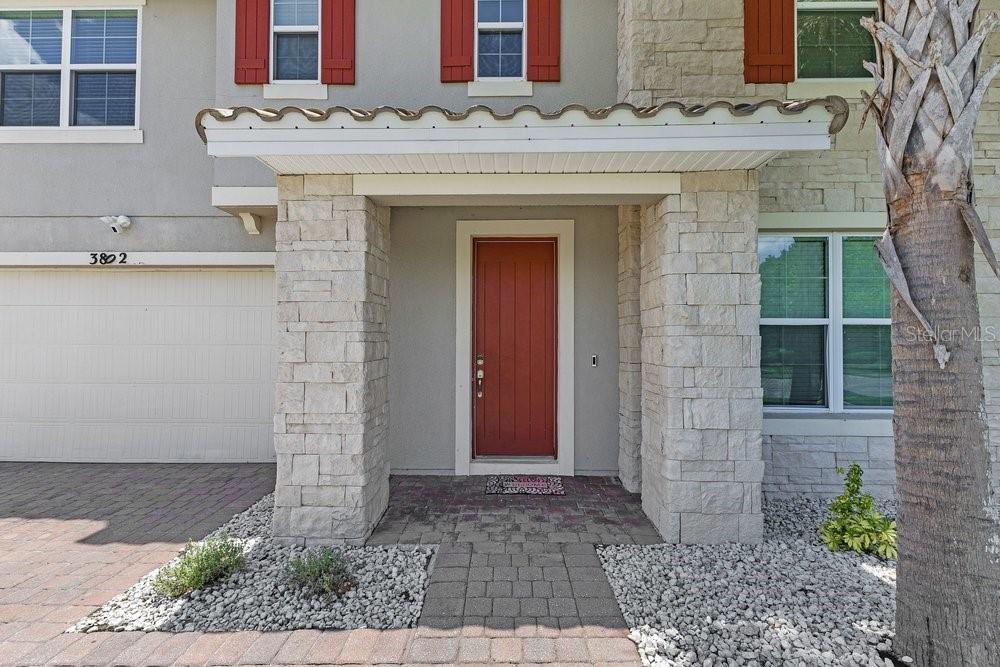 A two-story house exterior features a stone-accented entryway, a red front door, and shutters — 3802 CARRICK BEND DRIVE, KISSIMMEE, FL