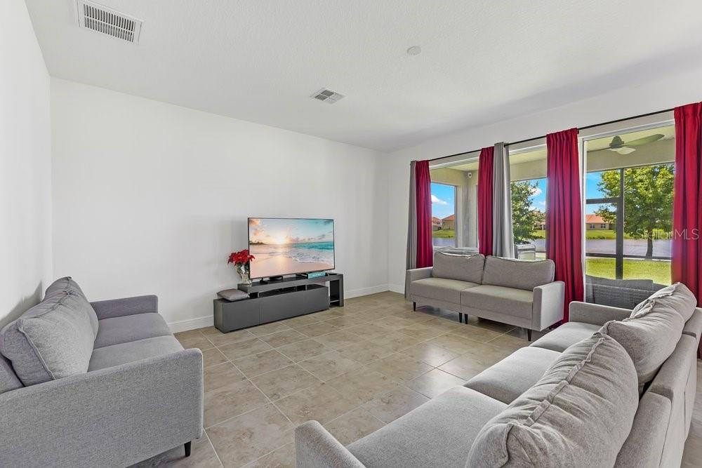 A living room features light tile floors, three gray sofas, and large windows with red curtains — 3802 CARRICK BEND DRIVE, KISSIMMEE, FL
