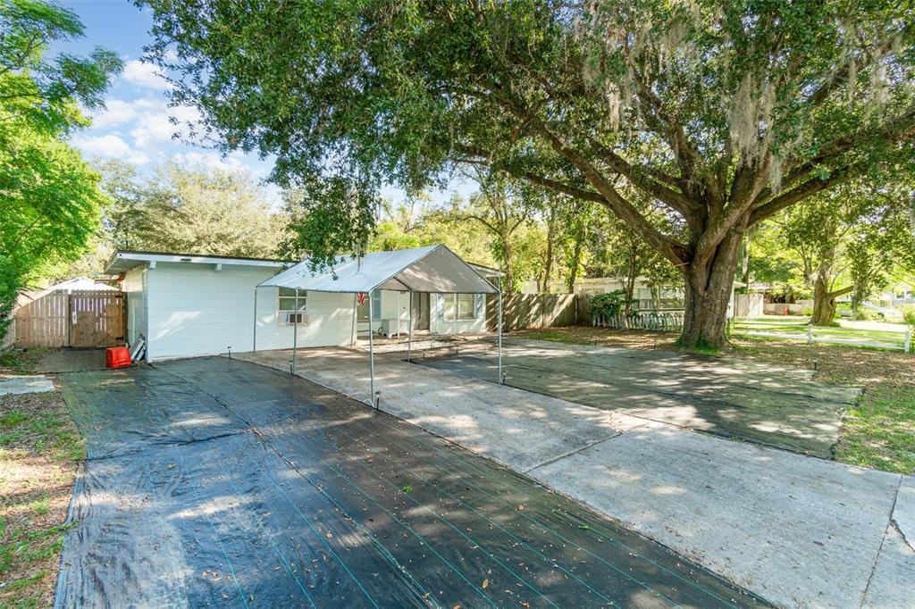 A single-story house with a metal carport and a large tree in the front yard — 306 FAIRMONT DRIVE, SANFORD, FL