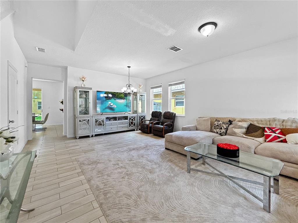 A living room features light tile flooring, a large sectional sofa, and a media console — 16100 YELLOWEYED DRIVE, CLERMONT, FL