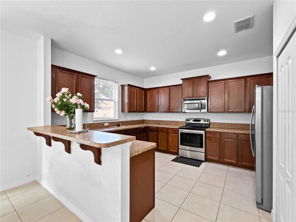 A kitchen features dark wood cabinets, stainless steel appliances, and a breakfast bar with countertops — 16100 YELLOWEYED DRIVE, CLERMONT, FL