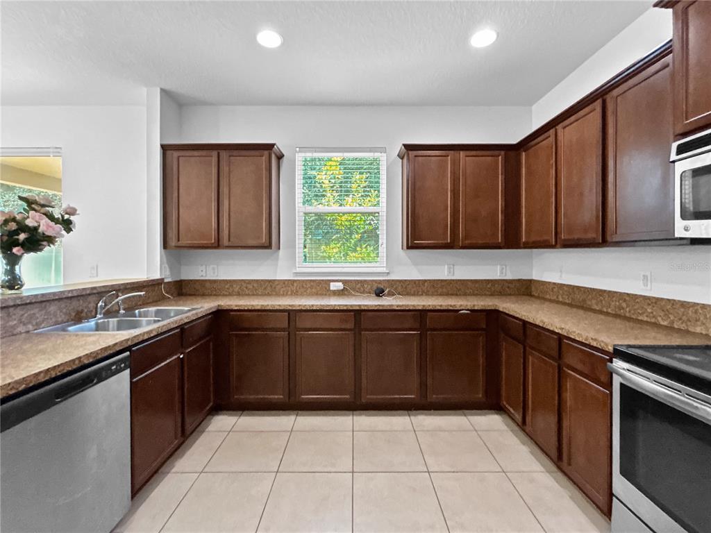 A kitchen features dark wood cabinets, speckled laminate countertops, stainless steel appliances, and tile flooring — 16100 YELLOWEYED DRIVE, CLERMONT, FL