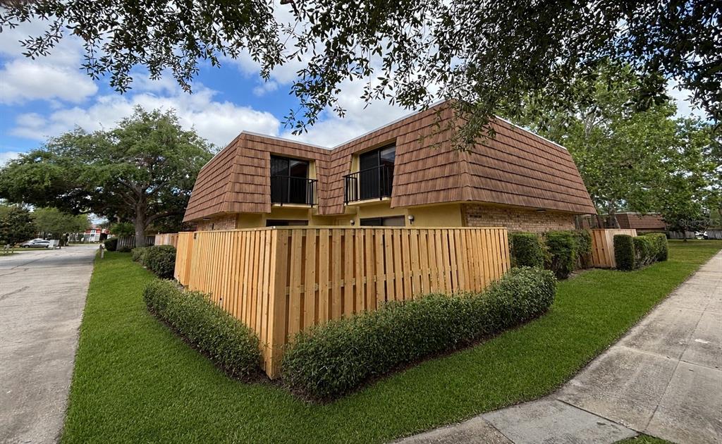 A two-story building with a mansard roof and a wooden privacy fence in the foreground — 5341 BAMBOO COURT UNIT 418, ORLANDO, FL