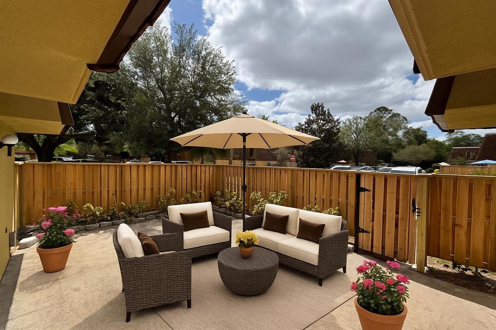 A patio features wicker furniture, a beige umbrella, and potted flowers against a wooden fence — 5341 BAMBOO COURT UNIT 418, ORLANDO, FL