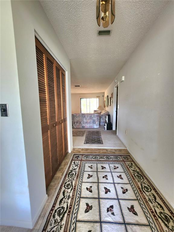 A hallway with a louvered closet door leads to a living area with carpeted floors — 12247 KATHERWOOD STREET, SPRING HILL, FL
