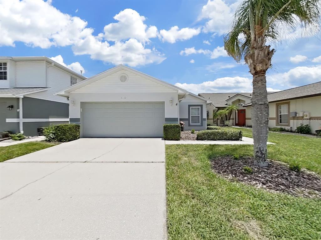 A single-story house with a two-car garage, a concrete driveway, and a palm tree — 6122 GENTLE BEN CIRCLE, WESLEY CHAPEL, FL