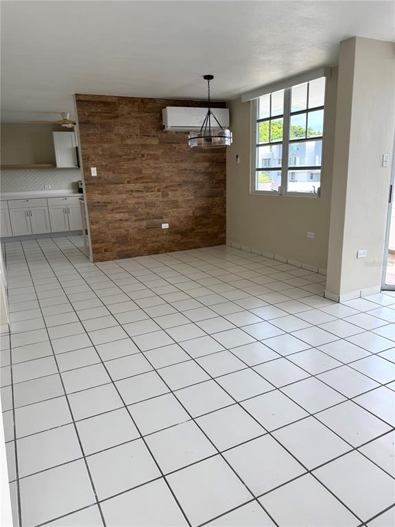 An open-concept dining area features white tile flooring, a wood-paneled accent wall, and a chandelier — 13 Camino Los Baez COND EL BOSQUE, GUAYNABO, PR