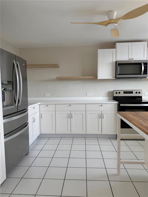 A kitchen features white cabinets, stainless steel appliances, open shelving, and white tile flooring — 13 Camino Los Baez COND EL BOSQUE, GUAYNABO, PR