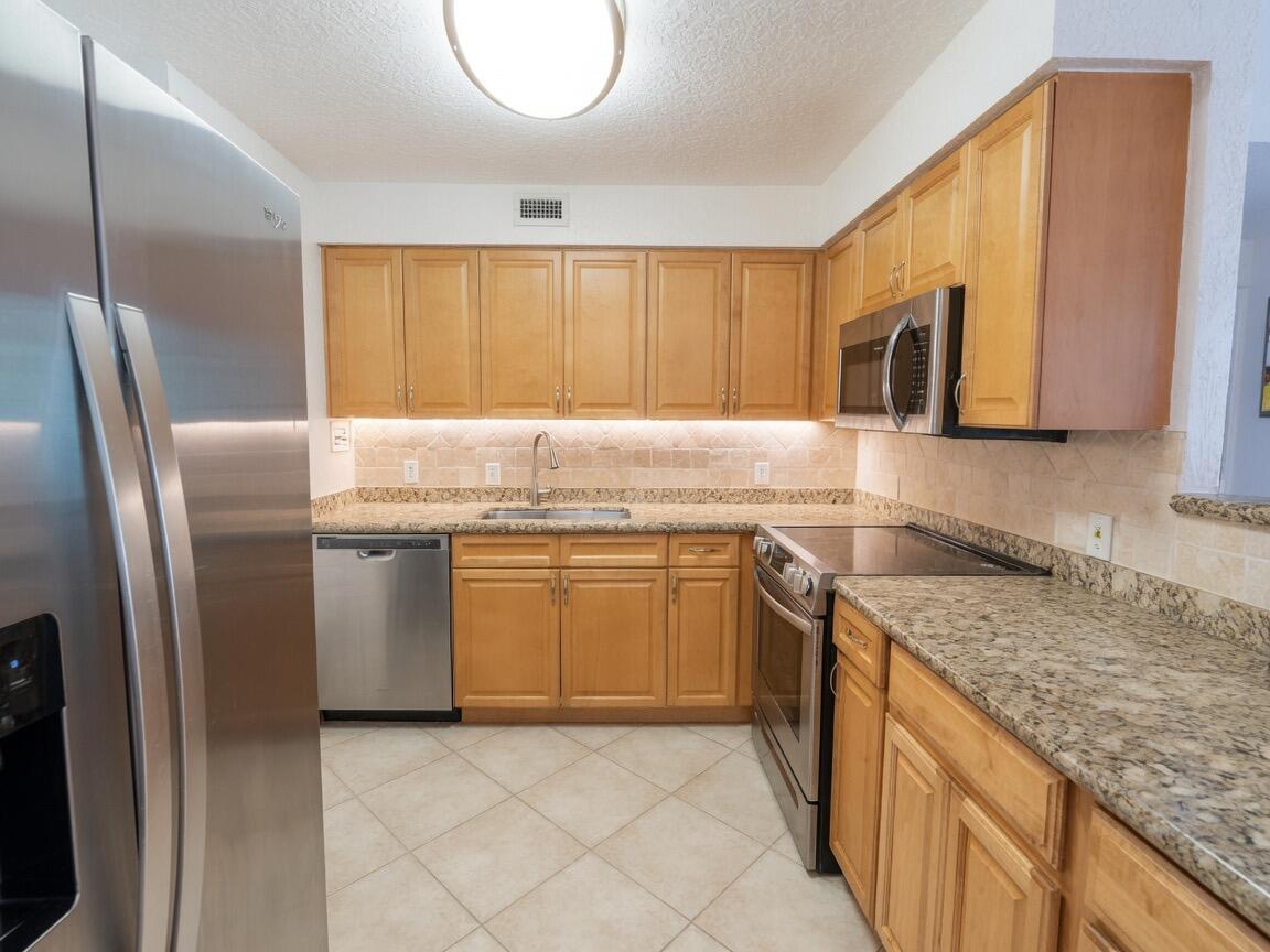 A kitchen features light wood cabinets, granite countertops, stainless steel appliances, and tile flooring — 1000 Spanish River Road # 4p, Boca Raton FL 33432, BOCA RATON, FL
