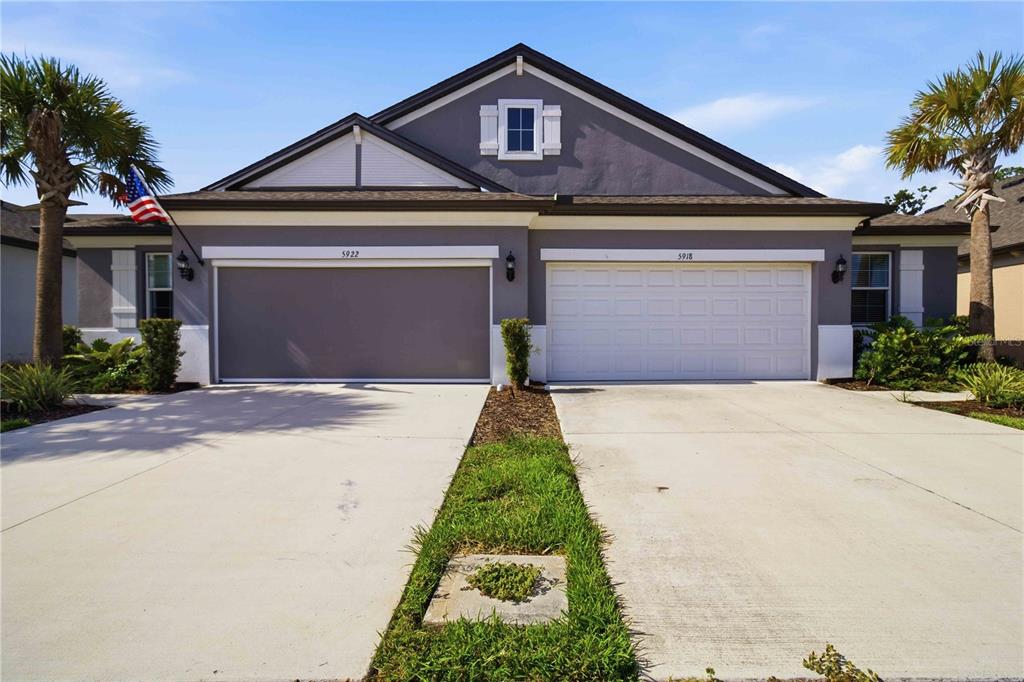 A single-story duplex with two garage doors, a gray exterior, and two palm trees — 5918 FIORE DRIVE, BRADENTON, FL