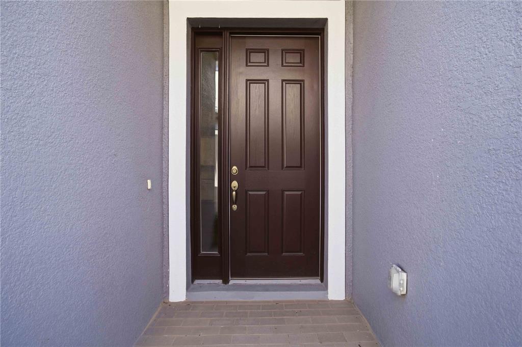 A dark brown front door with a side window is set in a purple stucco entryway — 5918 FIORE DRIVE, BRADENTON, FL