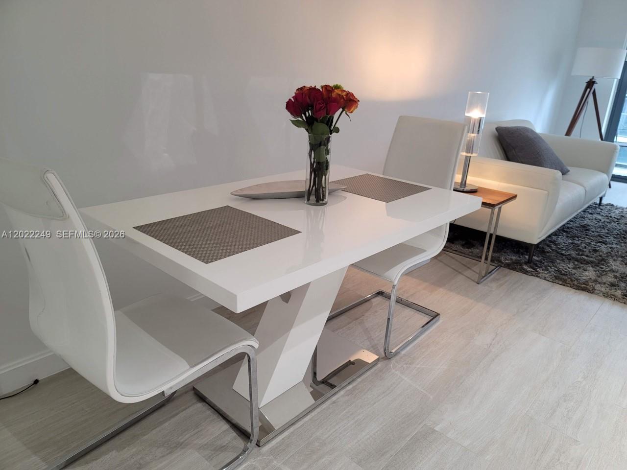 A modern dining area features a white table, two white chairs, and a nearby sofa — 55 SW 9th St # 2709, Miami FL 33130, MIAMI, FL
