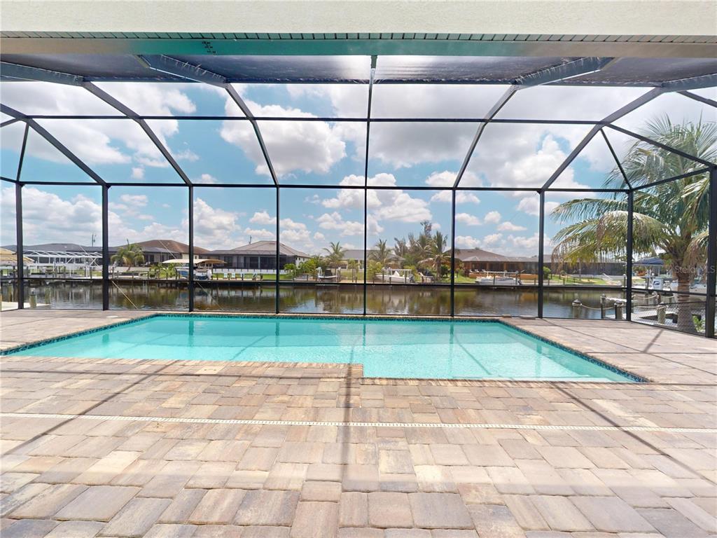 A screened-in pool patio features stone pavers overlooking a canal with docked boats — 229 NW 33RD AVENUE, CAPE CORAL, FL