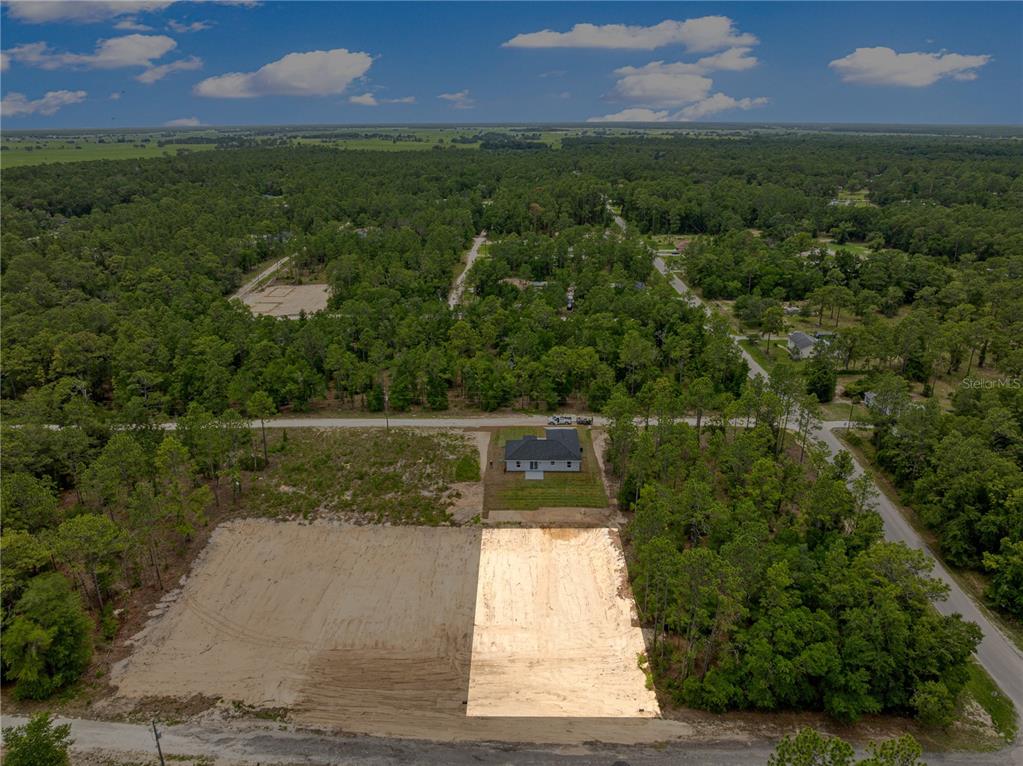 An aerial view shows a cleared sandy lot next to a newly constructed house — SW 38TH PLACE, OCALA, FL