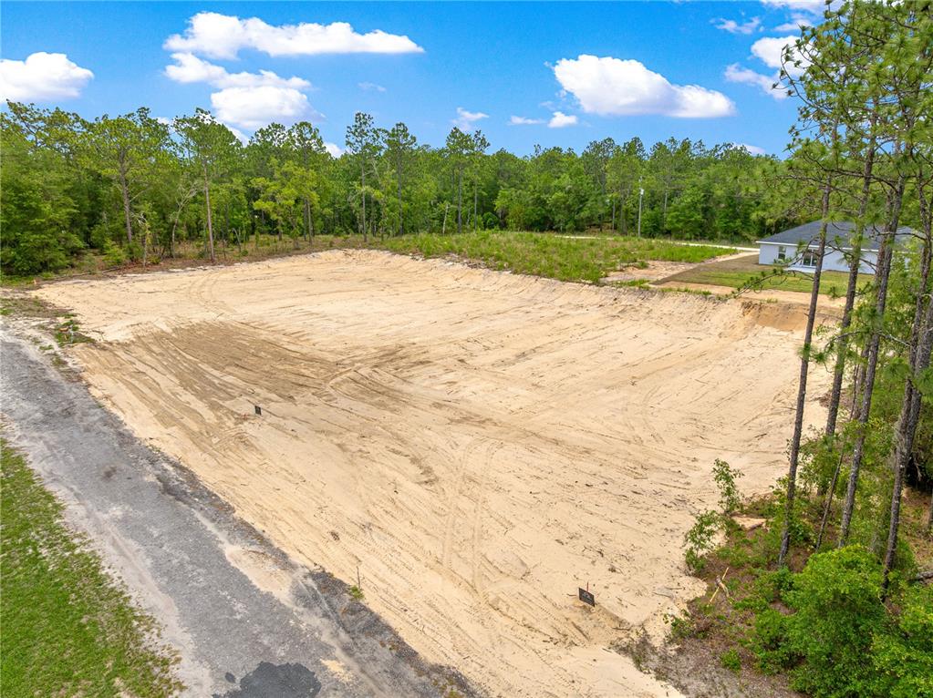 An elevated view of a cleared, sandy residential lot bordered by trees and a road — SW 38TH PLACE, OCALA, FL